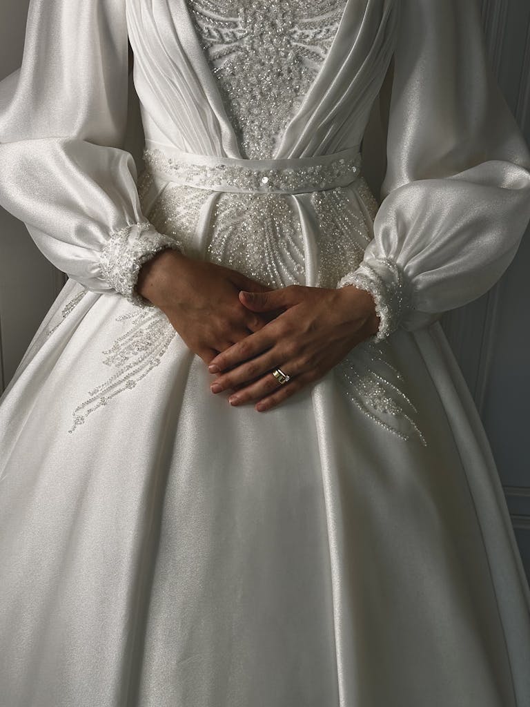 Close-up of an elegant bride in a white dress showcasing intricate details and a wedding ring.